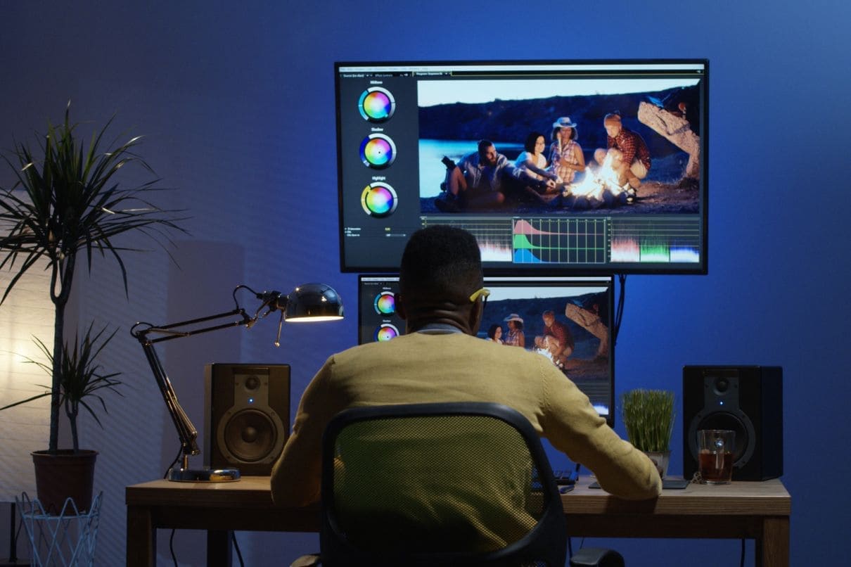 A man sitting at a desk with two monitors and a laptop, working diligently in a modern office setup.